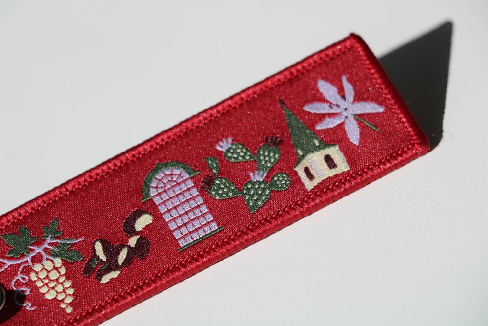 porte-cles-brode-motifs-valaisans-detail Détail d'un porte-clés brodé rouge avec raisin, châtaignes, cactus et clocher