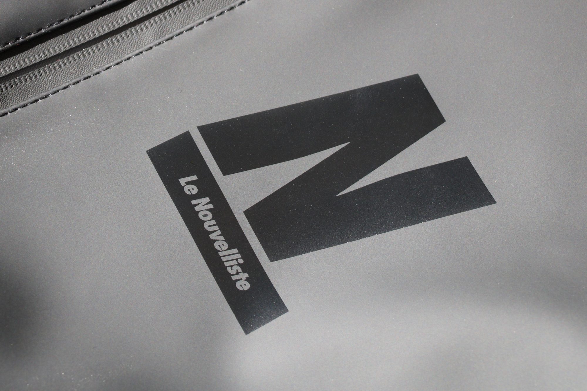 sac-a-dos-le-nouvelliste-logo-detail Détail du logo Le Nouvelliste imprimé sur un sac à dos gris